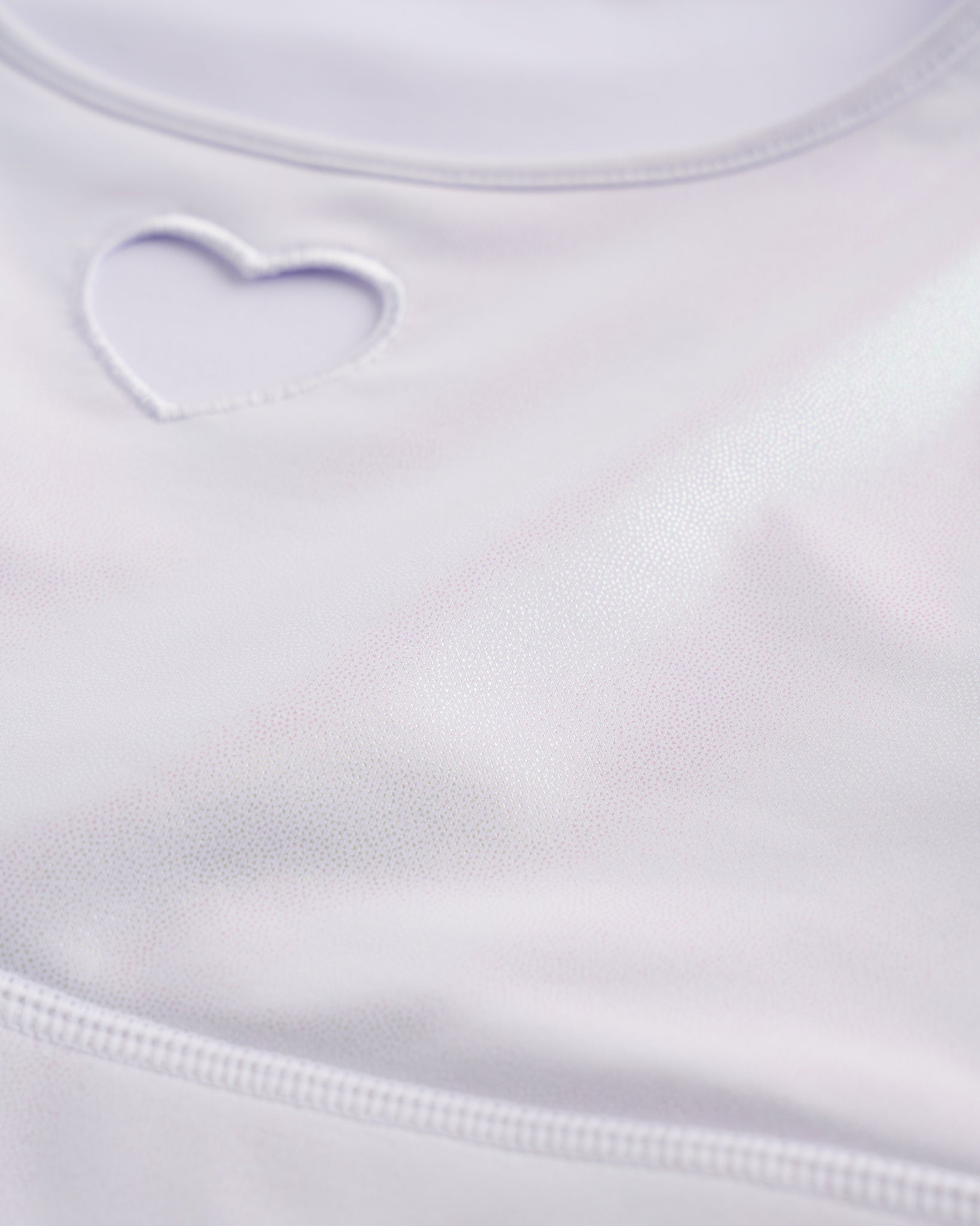 Close-up of white shimmer crop top showing heart cutout detail, smooth stitching, and iridescent fabric.
