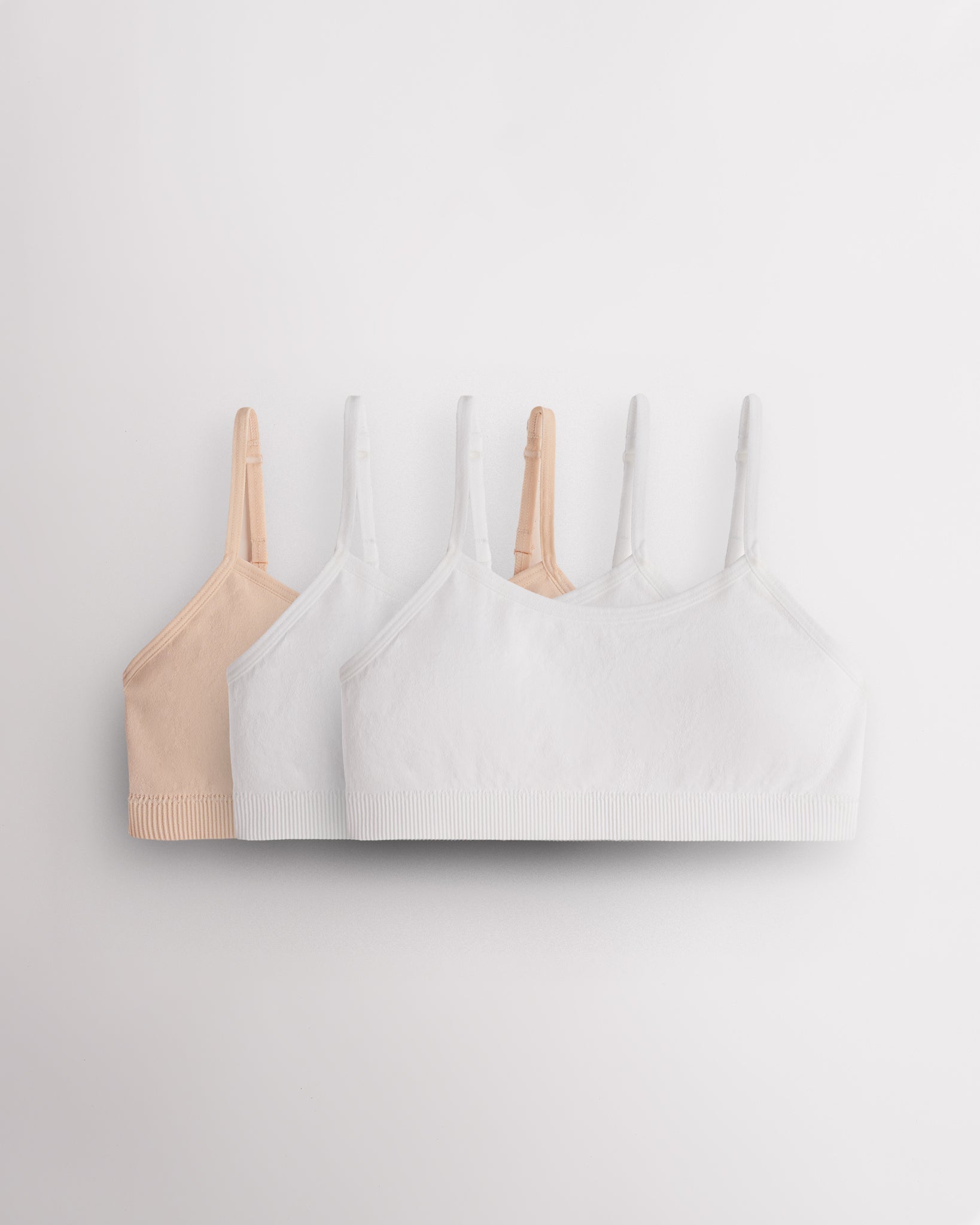 Three Stelle girls seamless cami bras in Soft Butter and white with slim adjustable straps and soft ribbed bands.