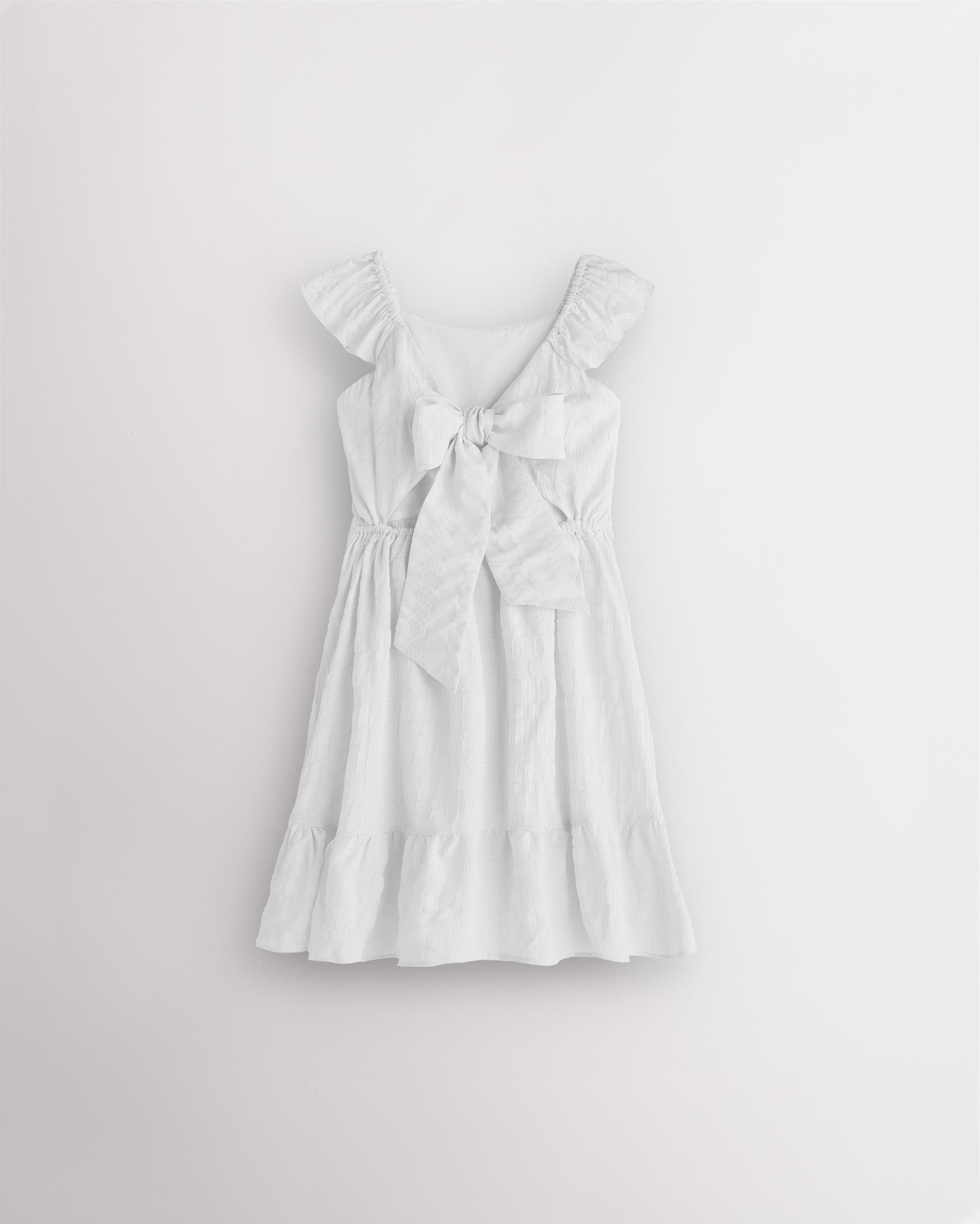 Girls white flutter sleeve sundress with adjustable bow back, smocked waist, and tiered skirt, back view showing bow detail