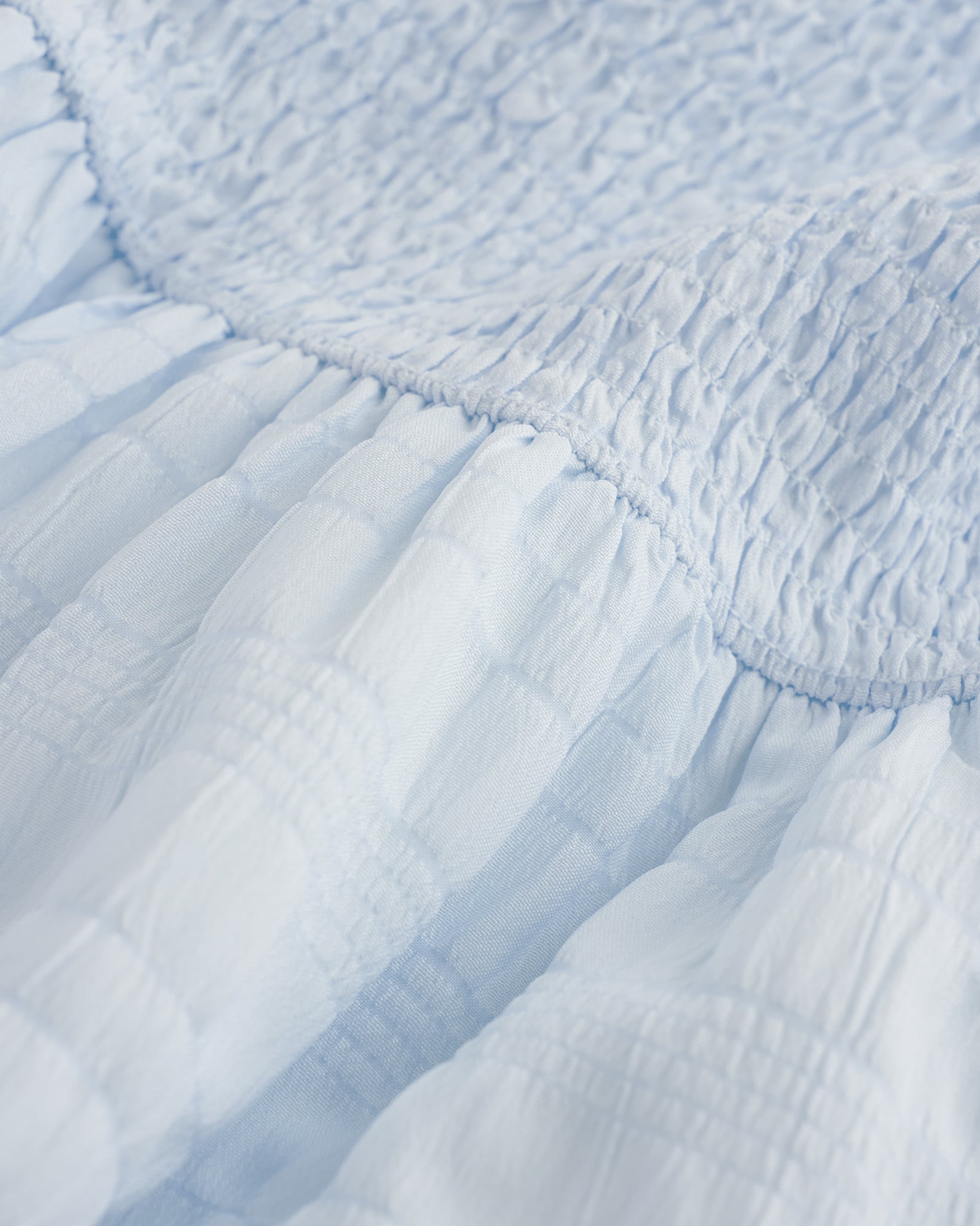 Close-up of light blue smocked fabric and gathered waist detail on Stelle girls dress.