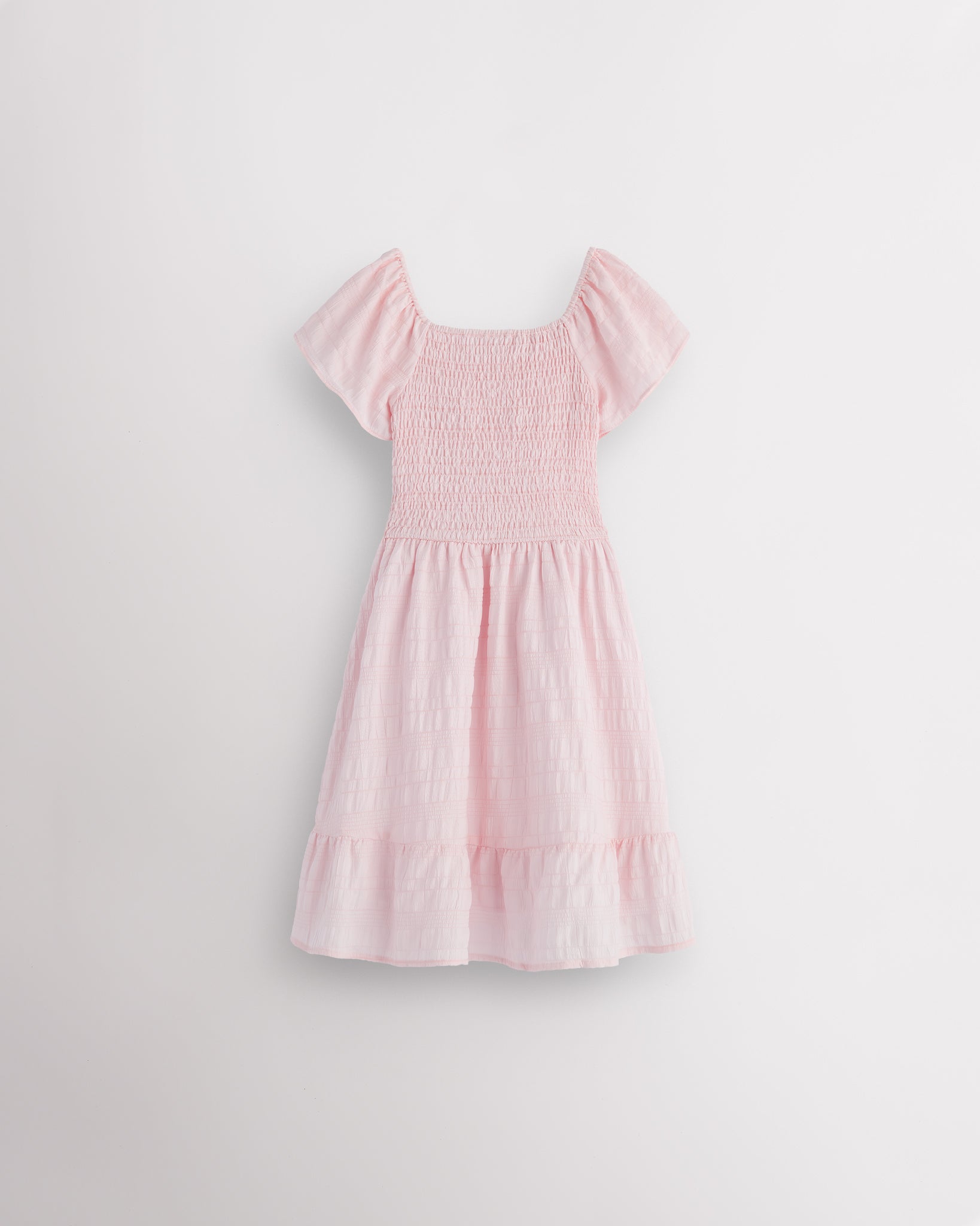 Back view of light pink girls summer dress showing smocked back, short sleeves, and soft gathered skirt.