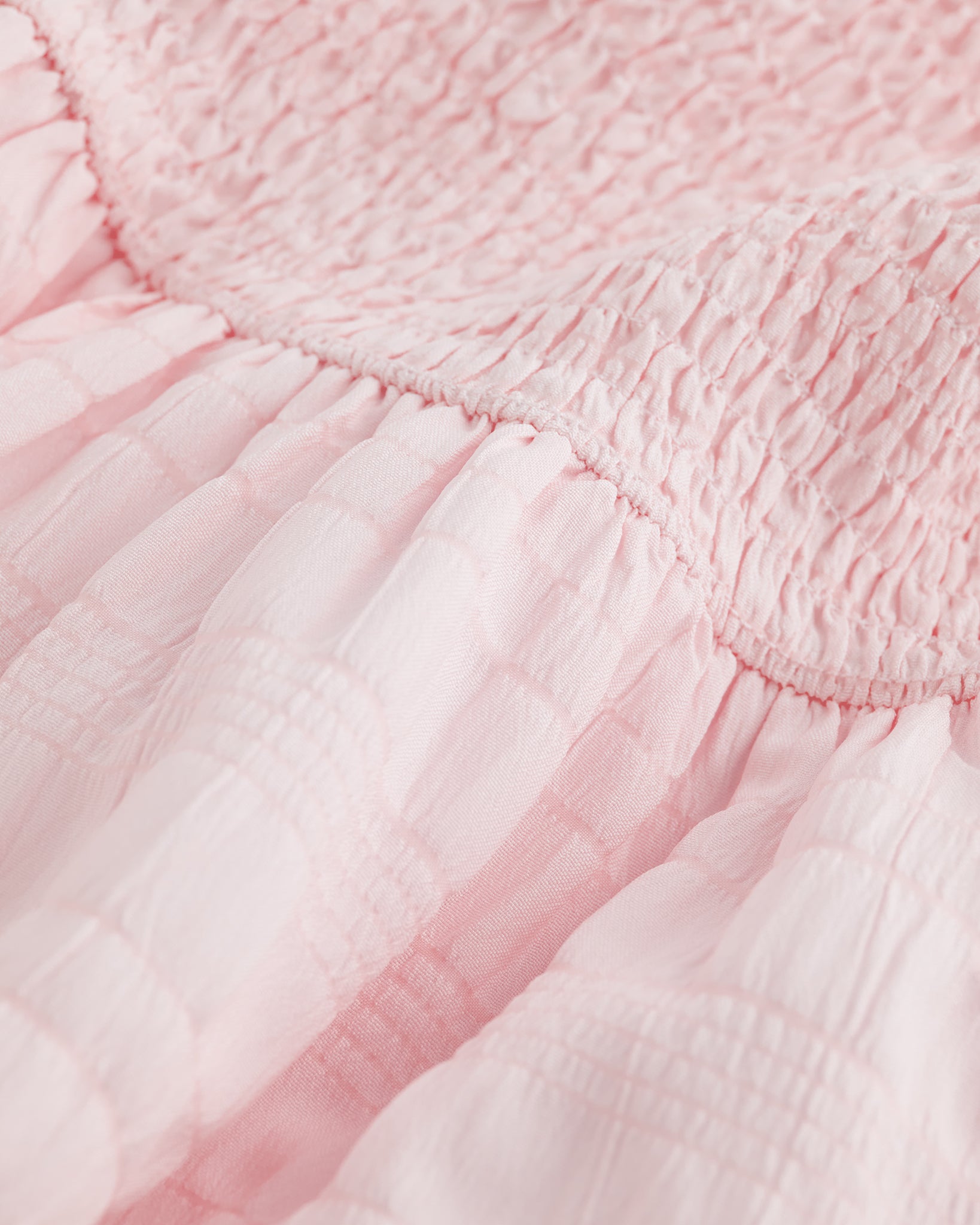 Close-up of light pink smocked fabric and gathered waist detail on Stelle girls dress.