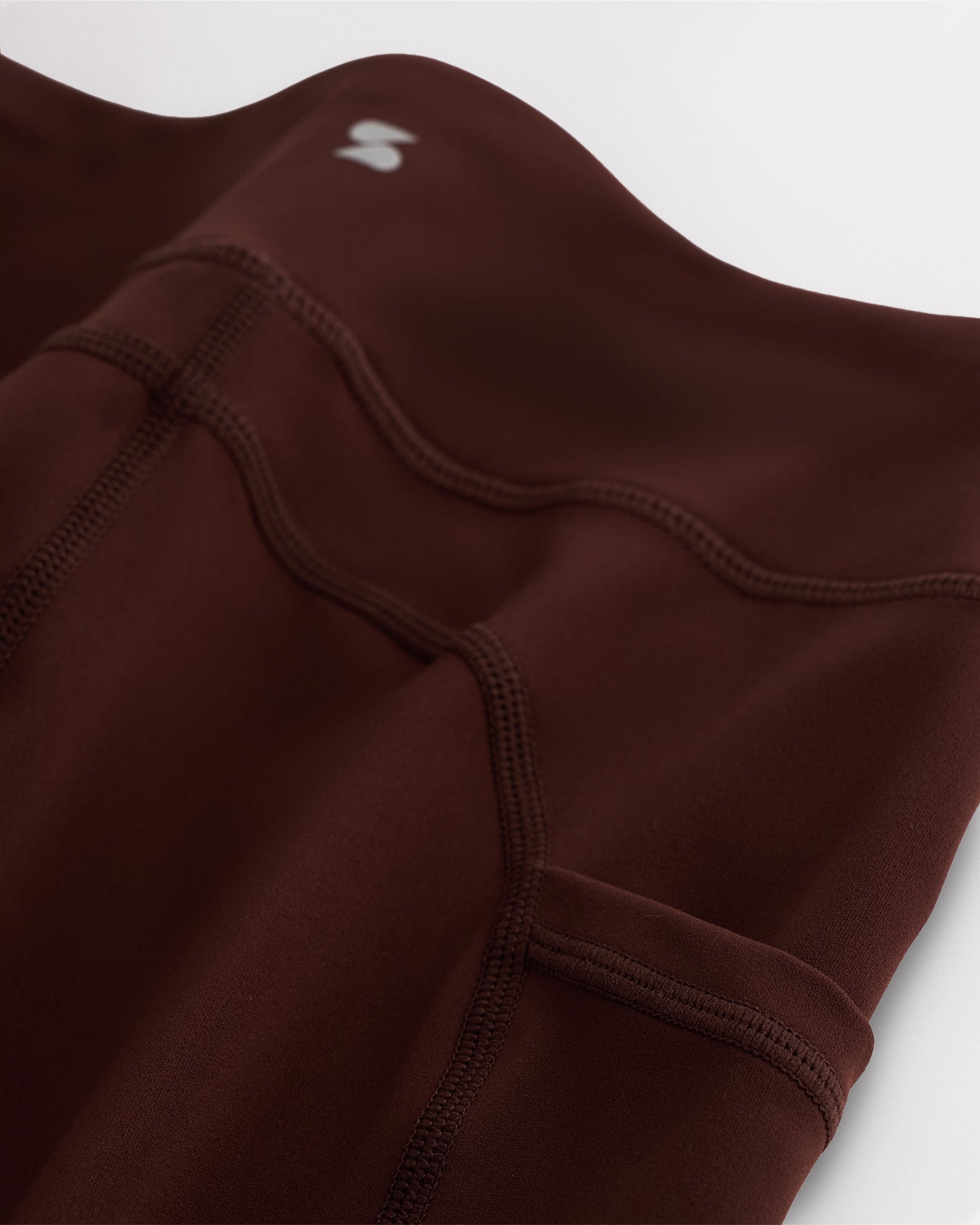 Close-up of coffee girls flare leggings showing soft 4-way stretch fabric, waistband seam, side pocket detail, and small Stelle logo.