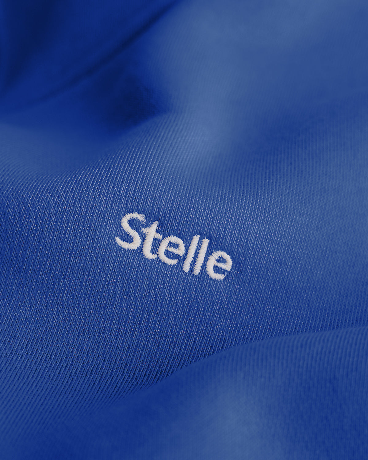 Close-up of the white embroidered Stelle logo on the cobalt blue fleece hoodie.