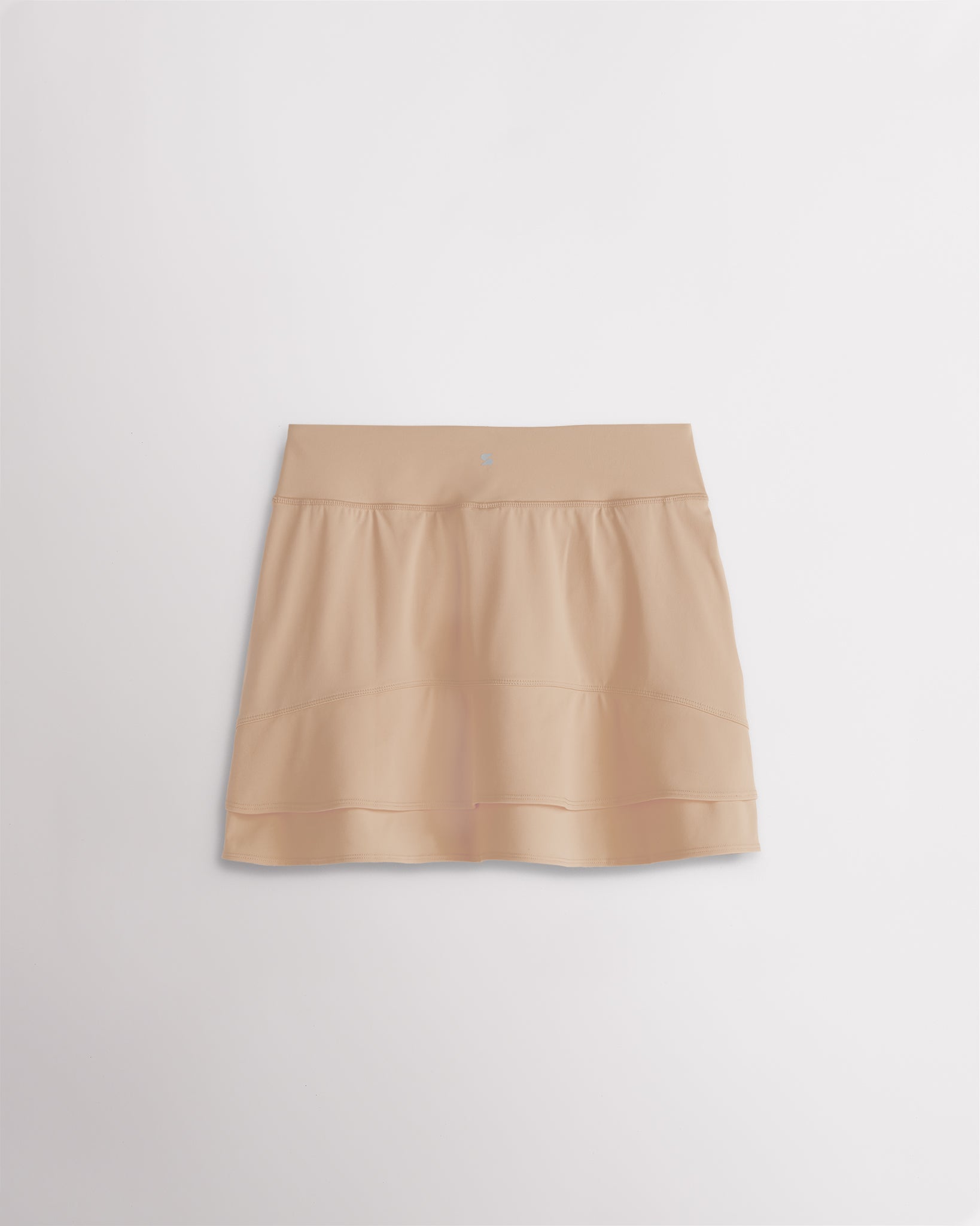 A quick-dry khaki tennis skirt with a smooth front, ruffle back hem, and built-in shorts with pockets for comfortable coverage on and off the court.