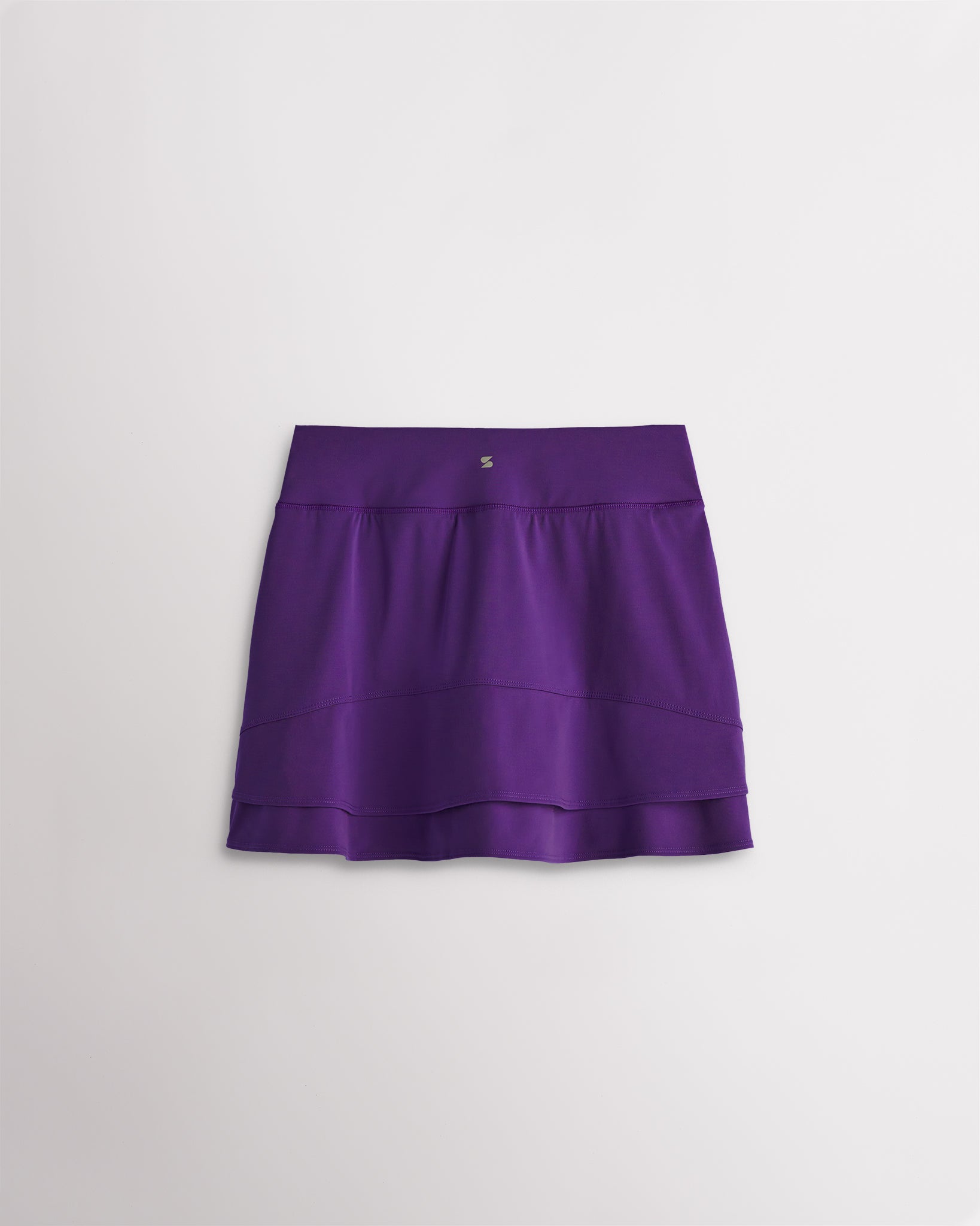 A quick-dry purple tennis skirt with a smooth front, ruffle back hem, and built-in shorts with pockets for comfortable coverage on and off the court.