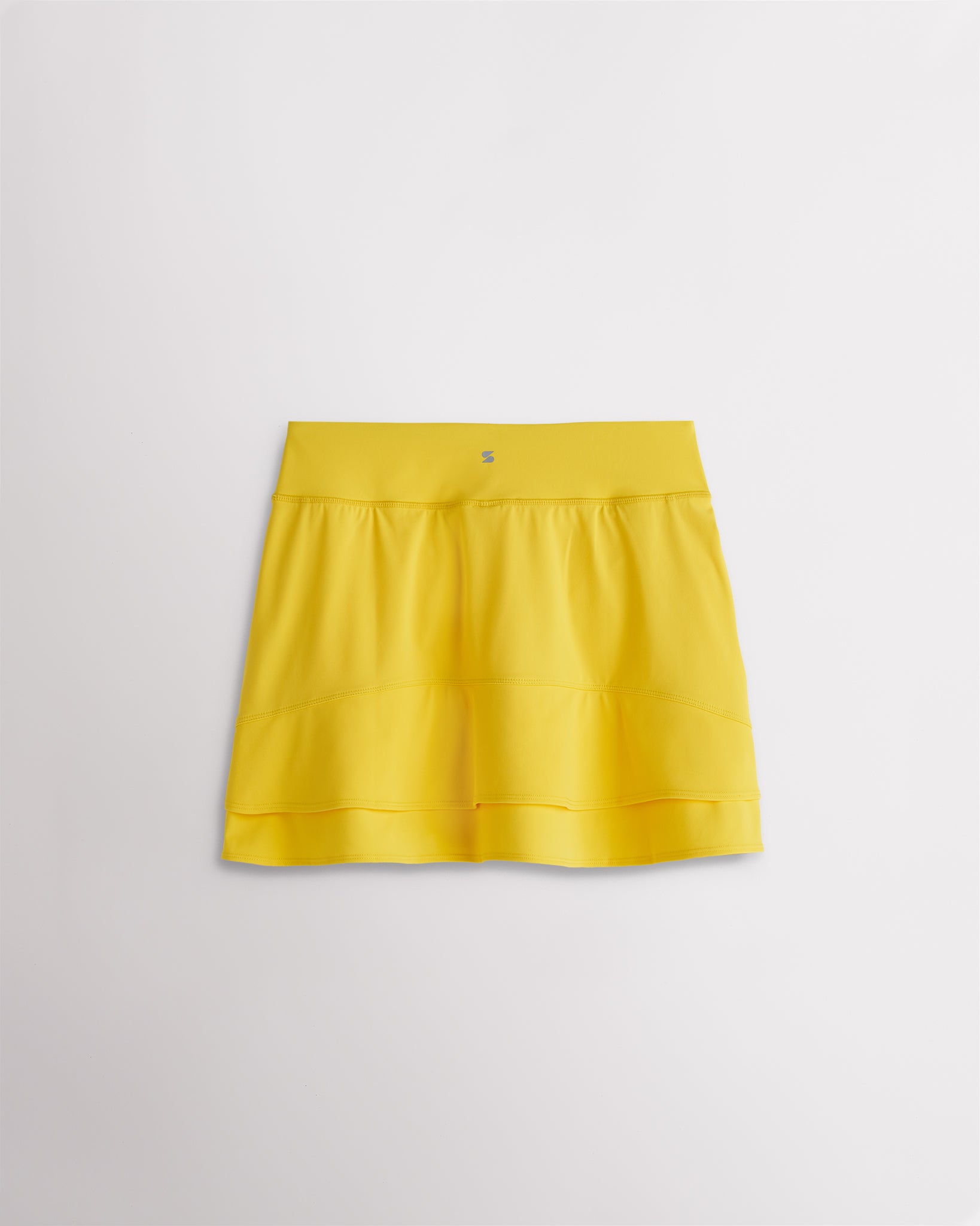 A quick-dry yellow tennis skirt with a smooth front, ruffle back hem, and built-in shorts with pockets for comfortable coverage on and off the court.