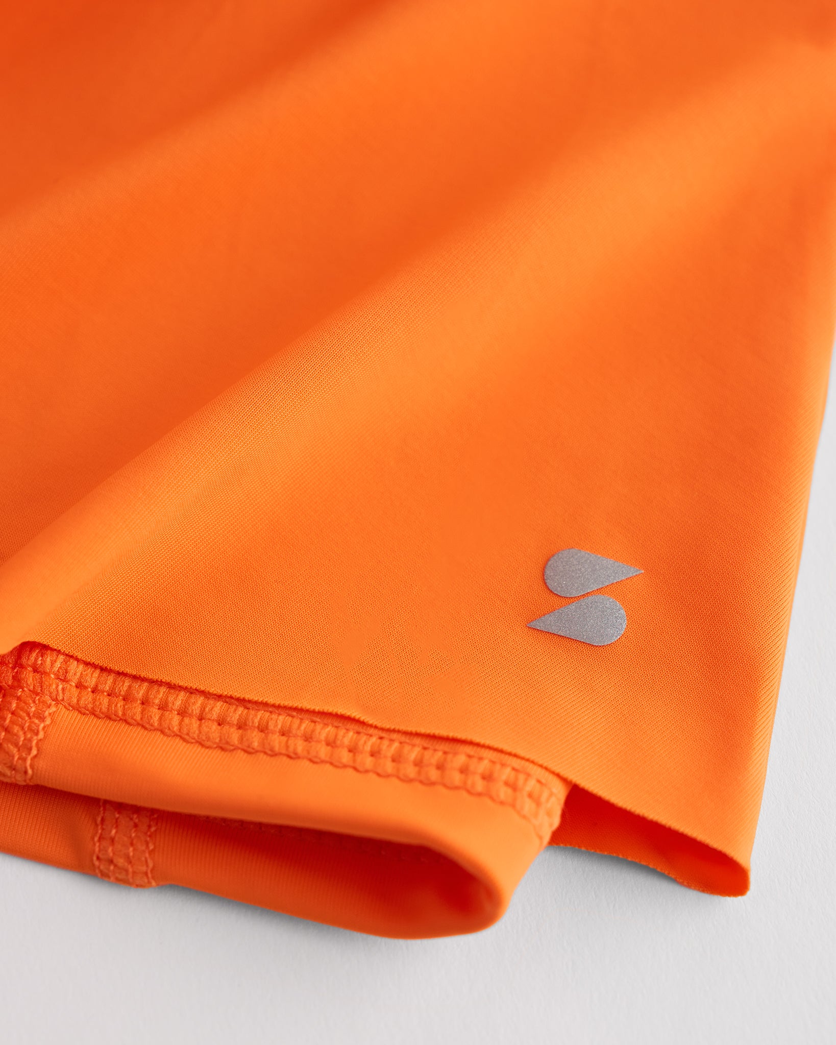 Close-up of orange Kids Let’s Bounce Shorts showing lightweight quick-dry fabric, hem stitching, and small Stelle logo detail.