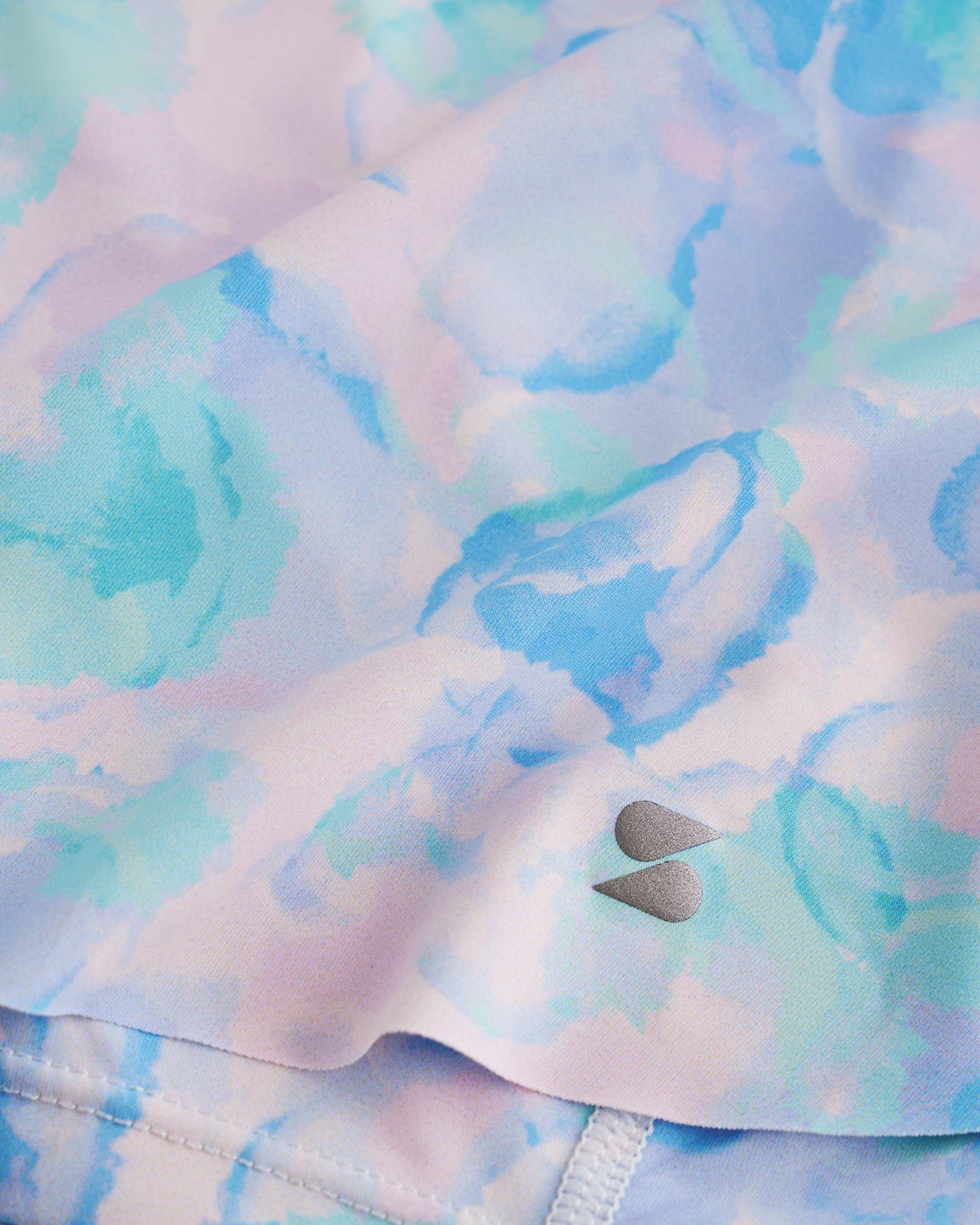 Close-up of Watercolor Bloom flowy shorts showing soft printed fabric, hem detail, and small Stelle logo.