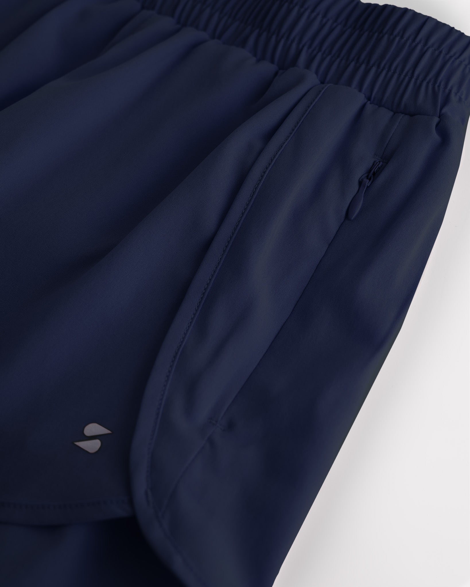 Close-up of girls navy running shorts showing elastic waistband, curved seam, and zipper pocket detail.