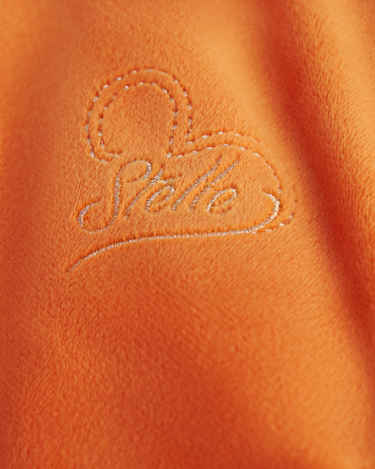 Close-up of the embroidered Stelle heart logo on the orange velour hoodie of the kids tracksuit set.