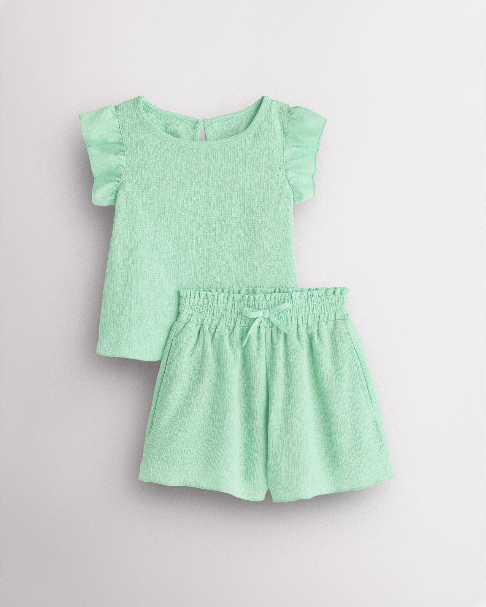 Girls green flutter sleeve summer outfit set with textured top, button-back detail, and matching elastic waist shorts with bow.