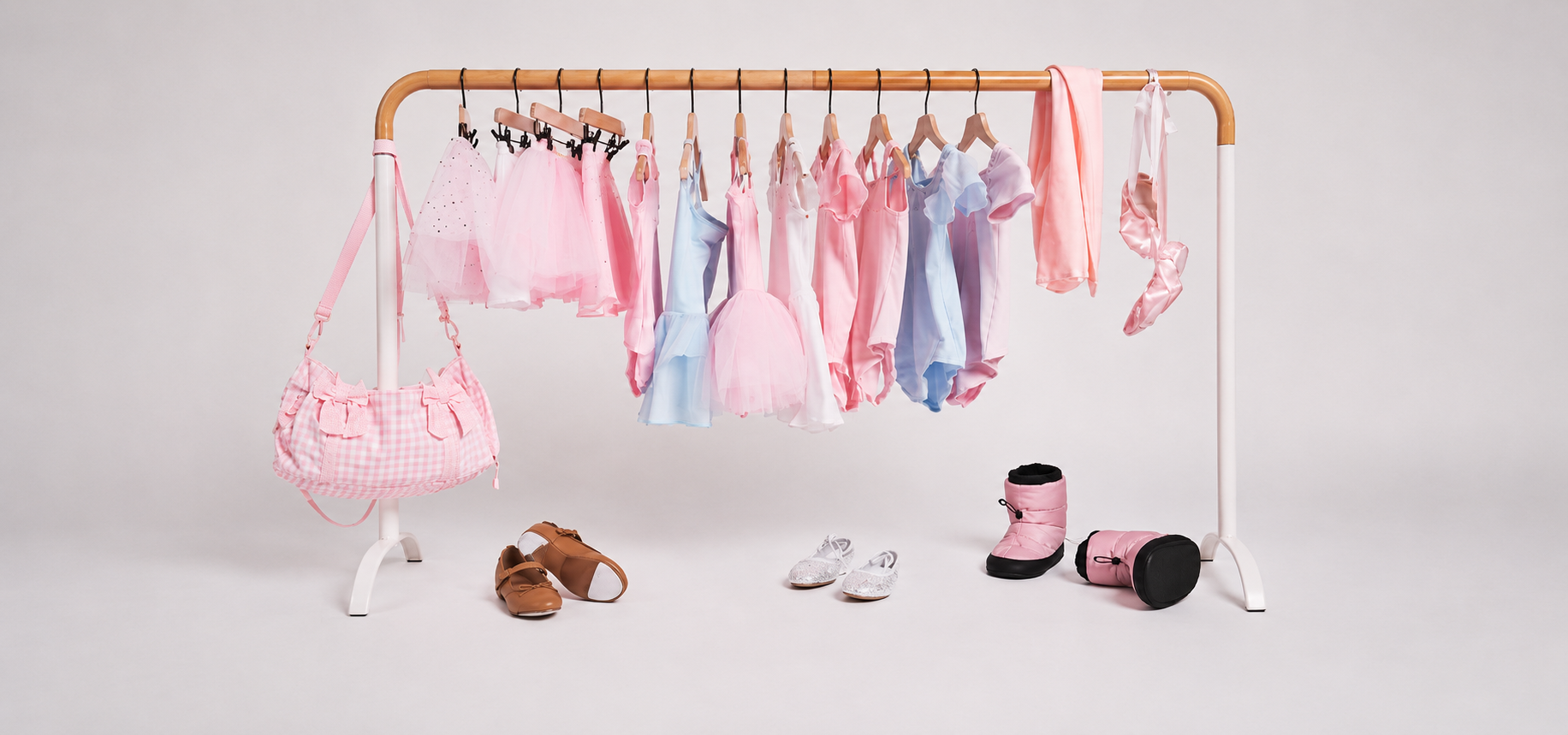 Pastel girls’ dancewear and ballet accessories displayed on a clothing rack, including leotards, tutus, ballet shoes, a dance bag, and warm-up booties.