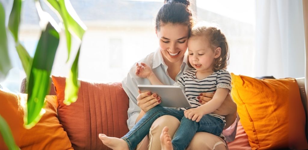 ChatGPT said: Mother and daughter sitting on a couch, smiling and looking at a tablet together.