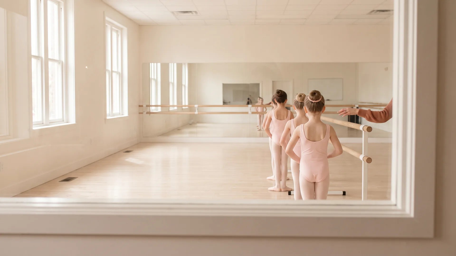 Young ballet students lined up at the barre during class, seen from the parent viewing window