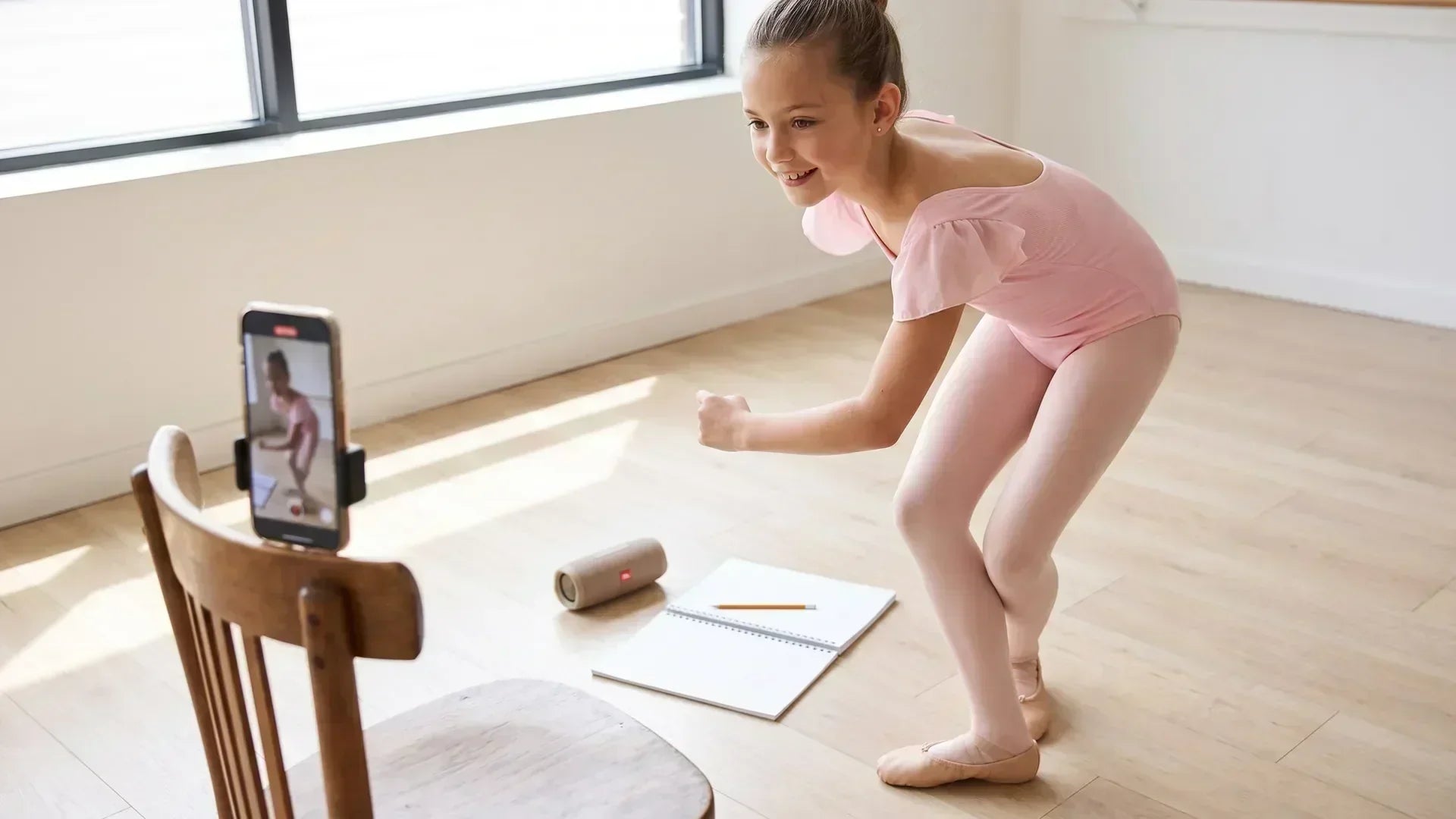 Young dancer marking out choreography counts in a bright studio with phone and notebook nearby