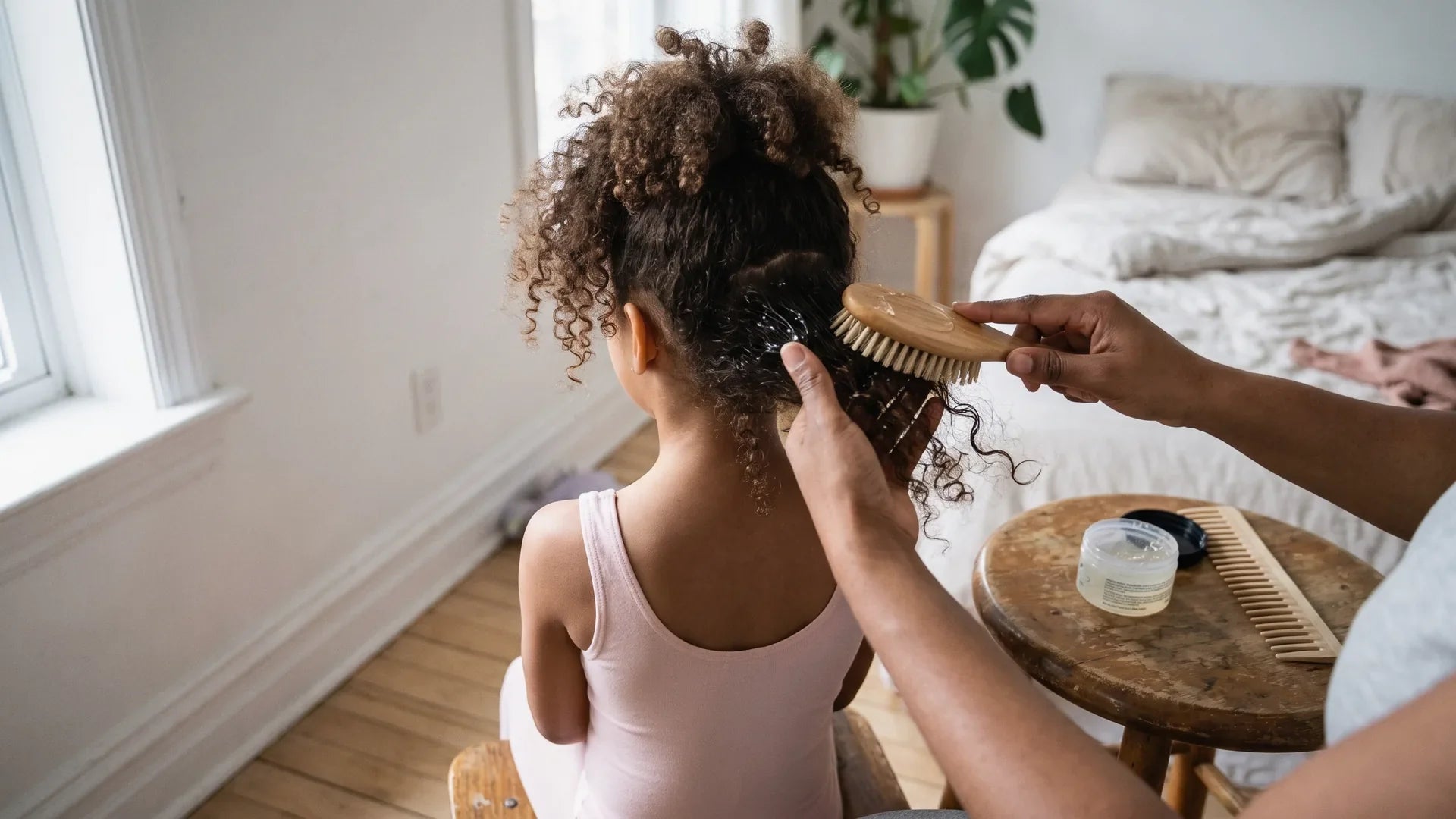 Parent smoothing gel into a girl's natural curls with a bristle brush to start a ballet bun on curly hair
