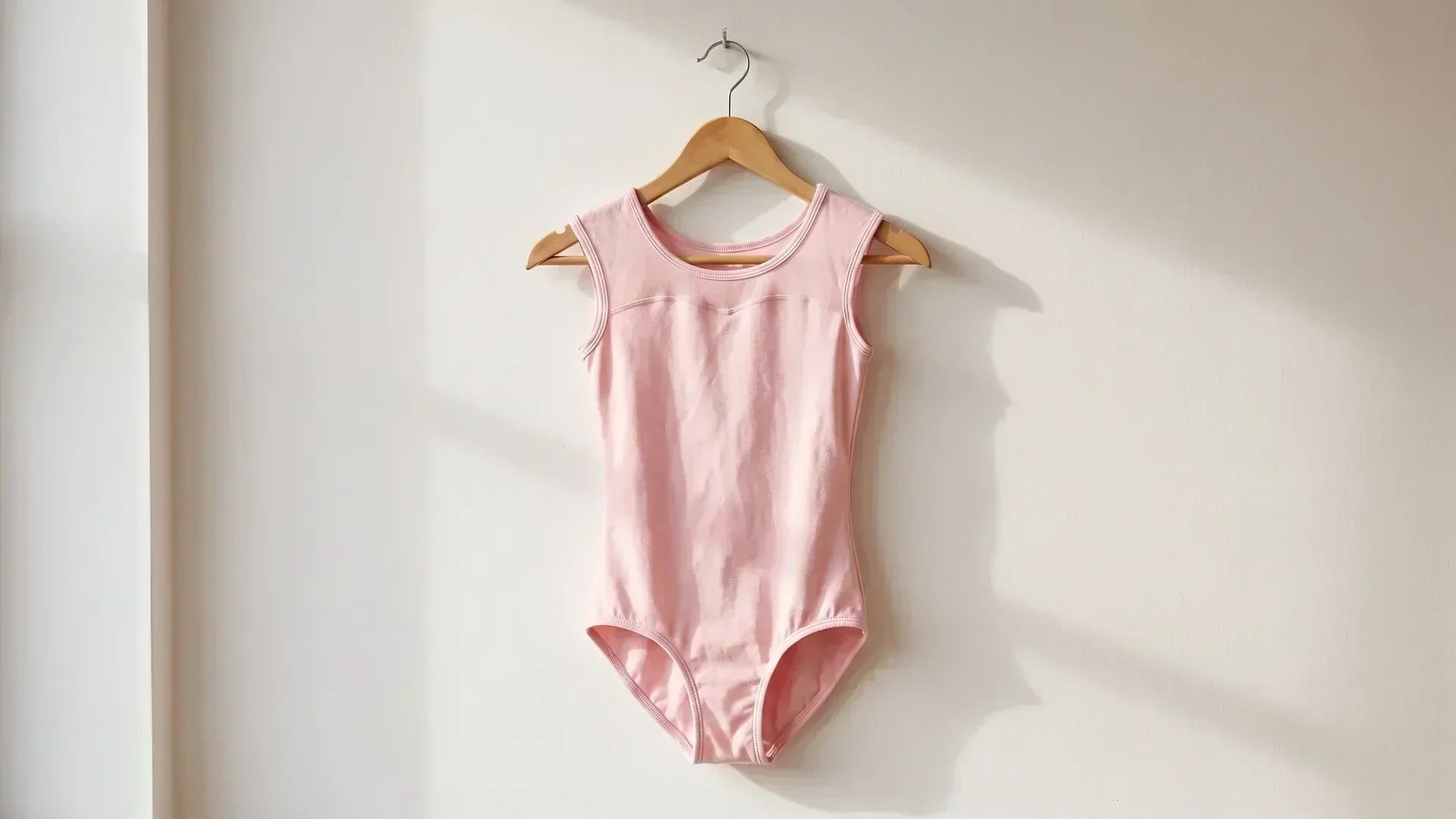 Classic pink camisole leotard on a wooden hanger against a studio wall