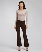 Woman wearing a beige long-sleeve top and brown flared pants on a light gray background