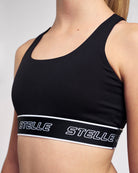Side view of the black Stelle sports bra with a scoop neckline and white logo underband.
