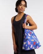 Model carrying Puppy Parade on Blue Stelle reusable grocery bag with puppy print over the shoulder, a lightweight foldable bag for markets and errands.