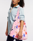 Model carrying Puppy Parade on Pink Stelle reusable grocery bag with puppy print over the shoulder, a lightweight foldable bag for markets and errands.