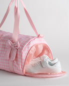 Kids pink gingham duffle bag with side shoe compartment holding sneakers, ideal for separating shoes from clothes.