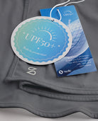 Close-up of grey sunscreen face mask showing UPF 50+ built-in protection tag, smooth fabric, and Stelle logo.