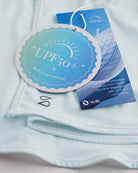 Close-up of Light Blue sunscreen face mask showing UPF 50+ built-in protection tag, smooth fabric, and Stelle logo.