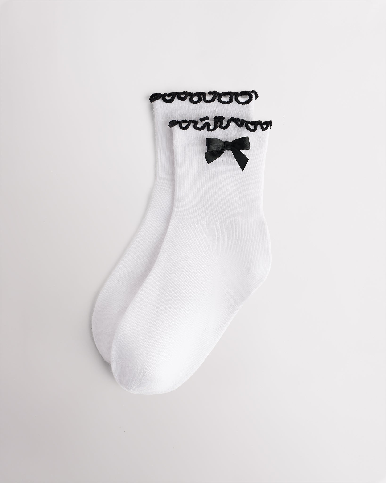 White kids socks with black ribbon bow, black lettuce-edge ruffle cuffs, and ribbed texture