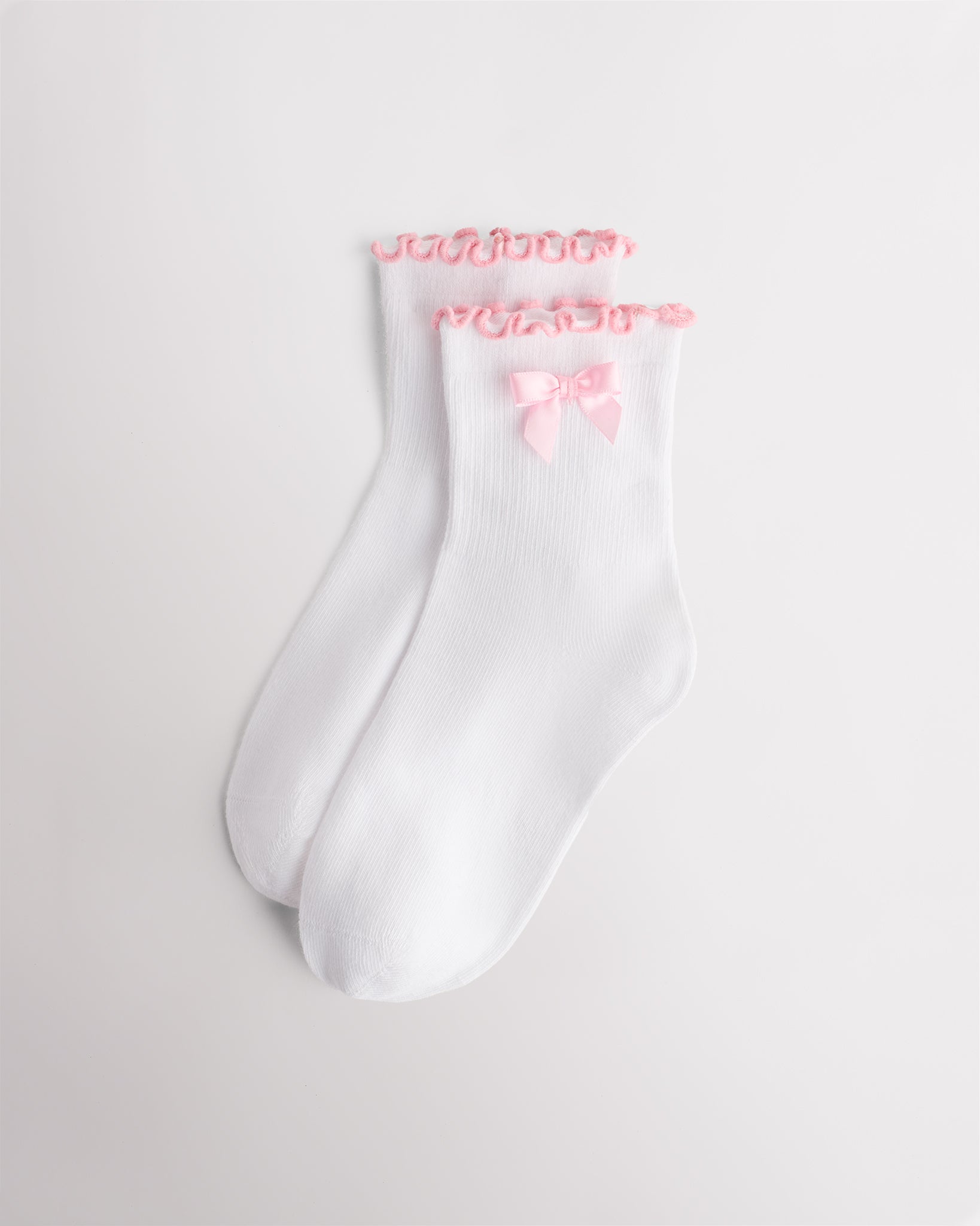 White kids socks with pink ribbon bow, pink lettuce-edge ruffle cuffs, and ribbed texture
