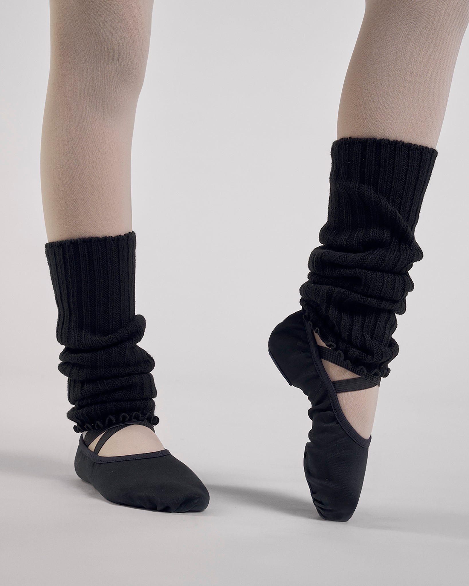 Black kids ballet leg warmers worn over tights with black ballet shoes during a ballet pose.