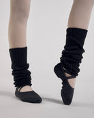 Black kids ballet leg warmers worn over tights with black ballet shoes during a ballet pose.