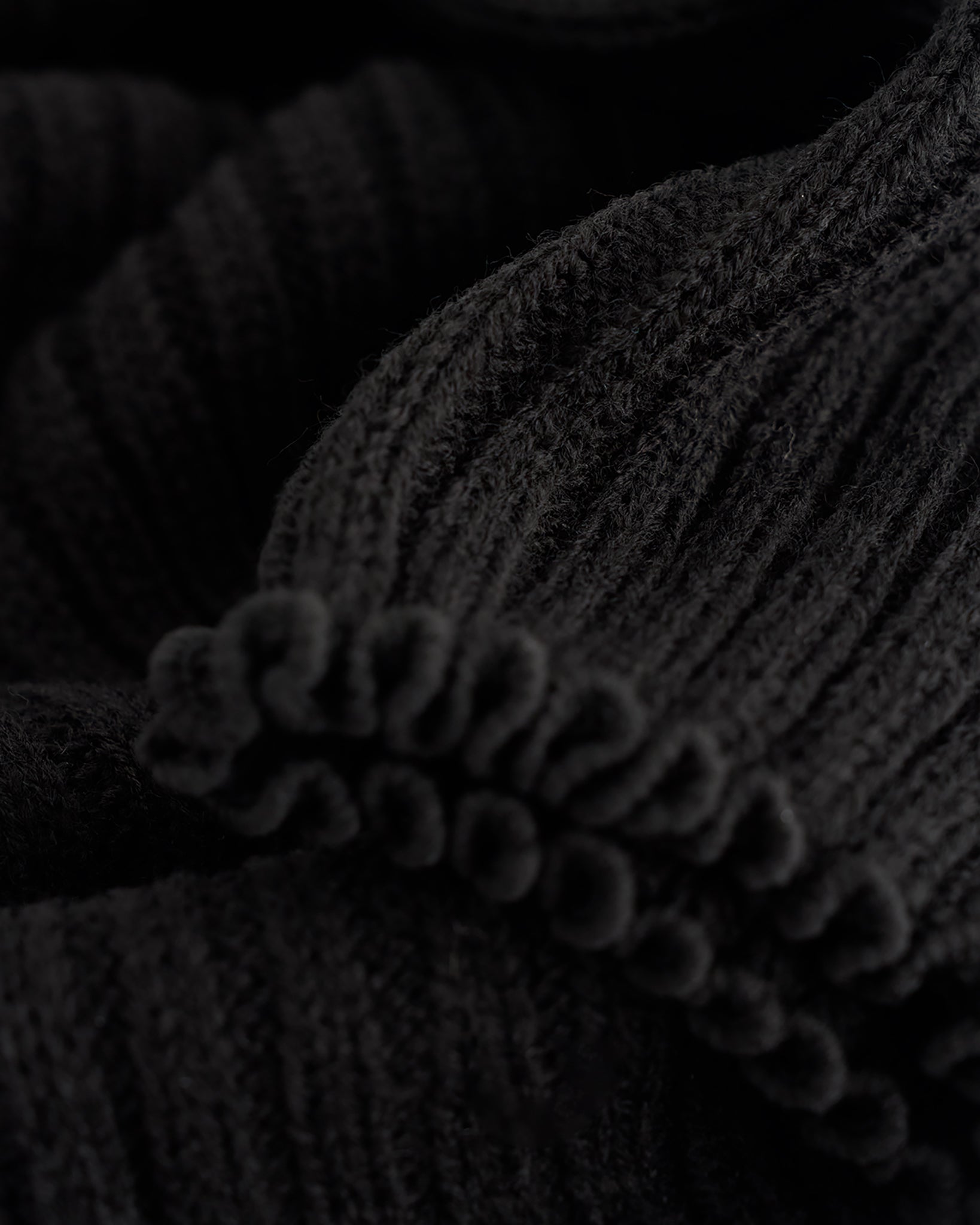 Close-up of black ballet leg warmers showing soft knit texture and delicate lettuce-edge trim.