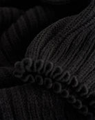 Close-up of black ballet leg warmers showing soft knit texture and delicate lettuce-edge trim.