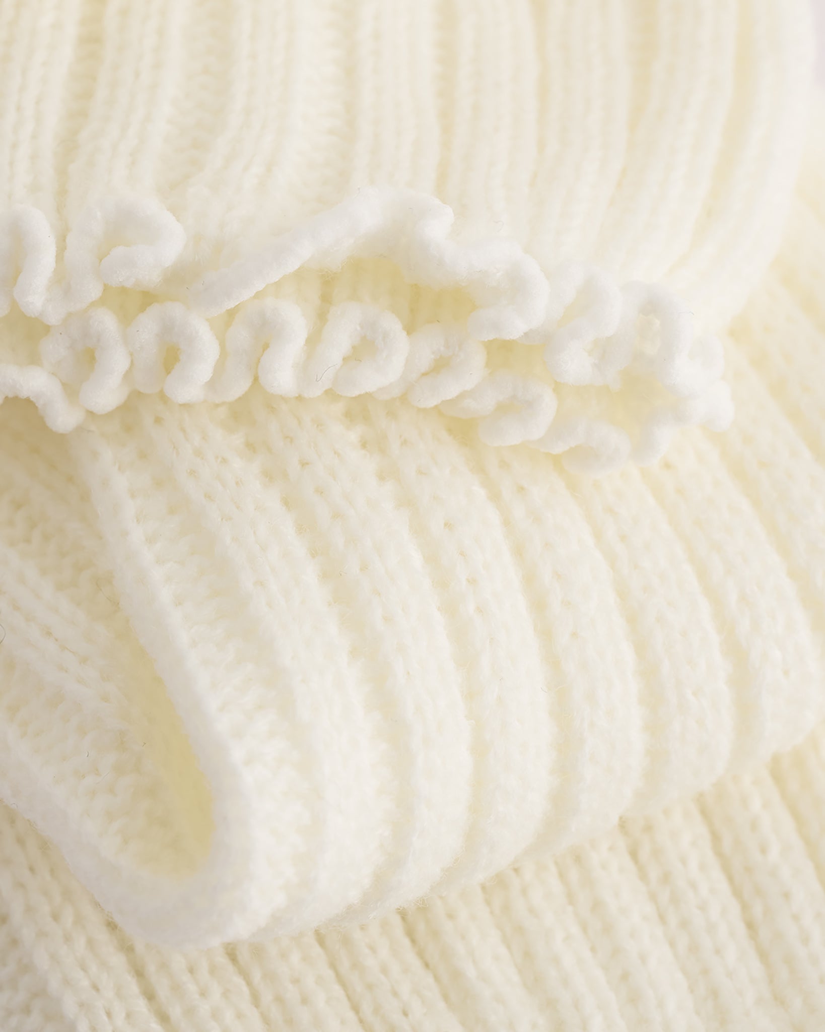 Close-up of creme ballet leg warmers showing soft knit texture and delicate lettuce-edge trim.