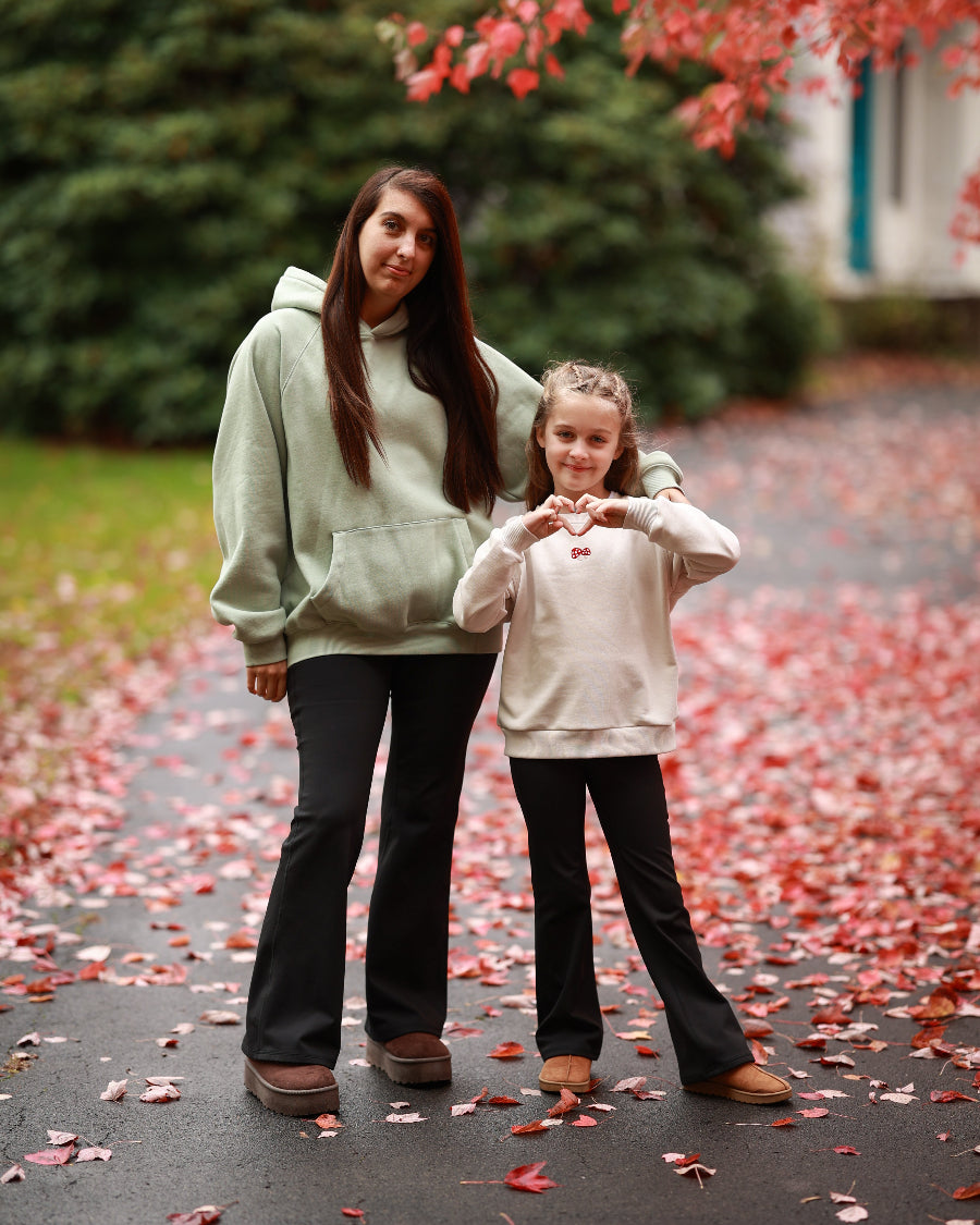 Woman and young girl standing on a path with red leaves, making heart shapes with their hands.
