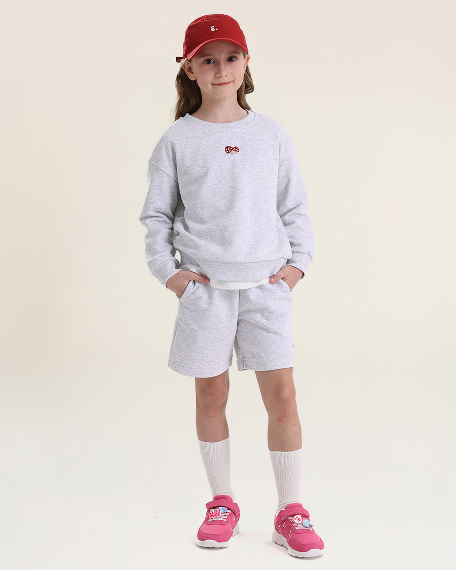 Child wearing a gray sweatshirt and shorts set with pink shoes on a white background