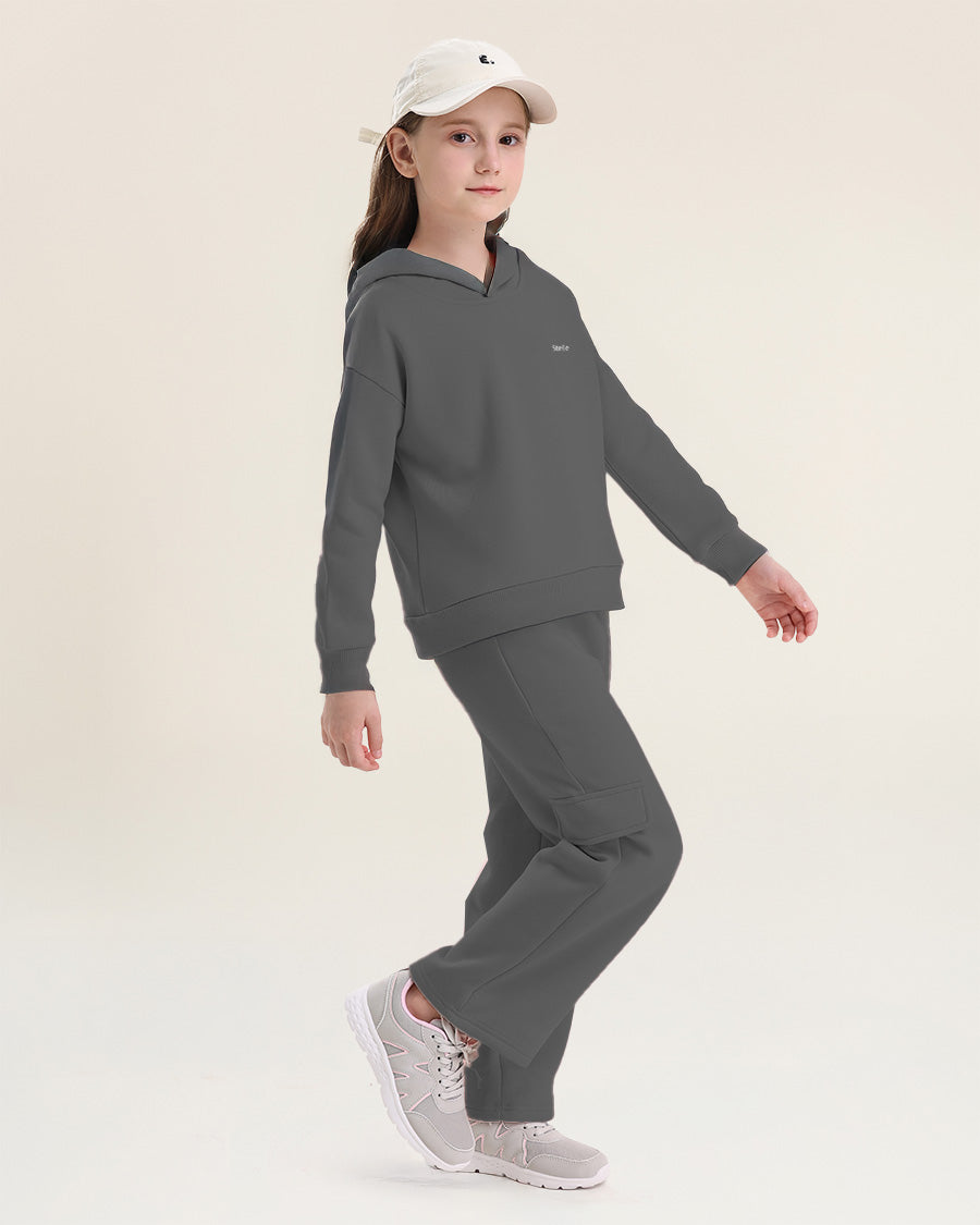 Child wearing a gray hoodie and pants set with a white cap on a beige background
