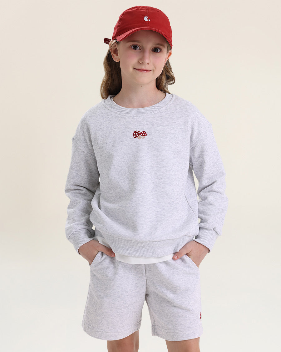Child wearing a gray sweatshirt and shorts set with a red cap on a beige background