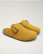 Pair of mustard yellow clogs with a gold buckle on a light gray background