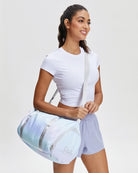 Woman holding a light blue duffel bag against a plain background