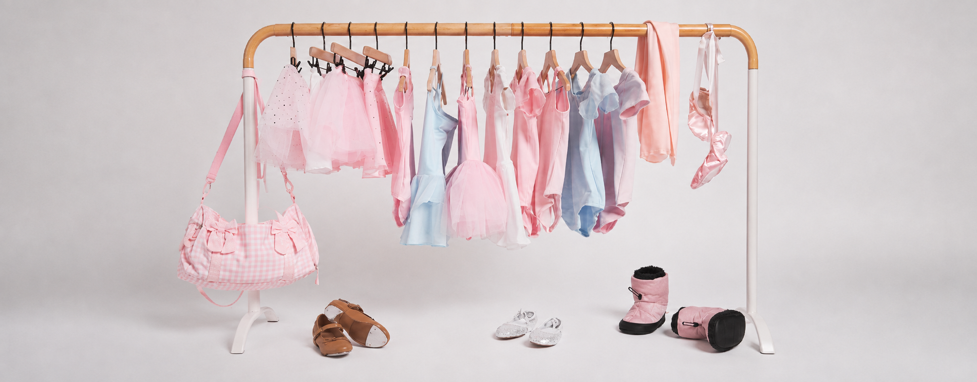 Pastel girls’ dancewear and ballet accessories displayed on a clothing rack, including leotards, tutus, ballet shoes, a dance bag, and warm-up booties.