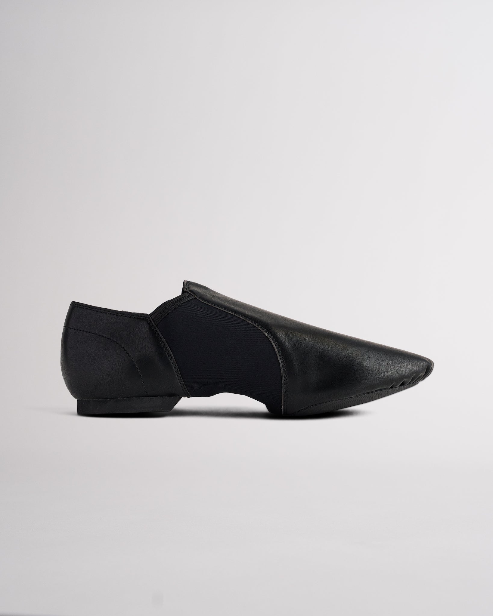Side view of black vegan leather jazz shoe showing slip-on design, stitched details, and flexible dance shoe shape.
