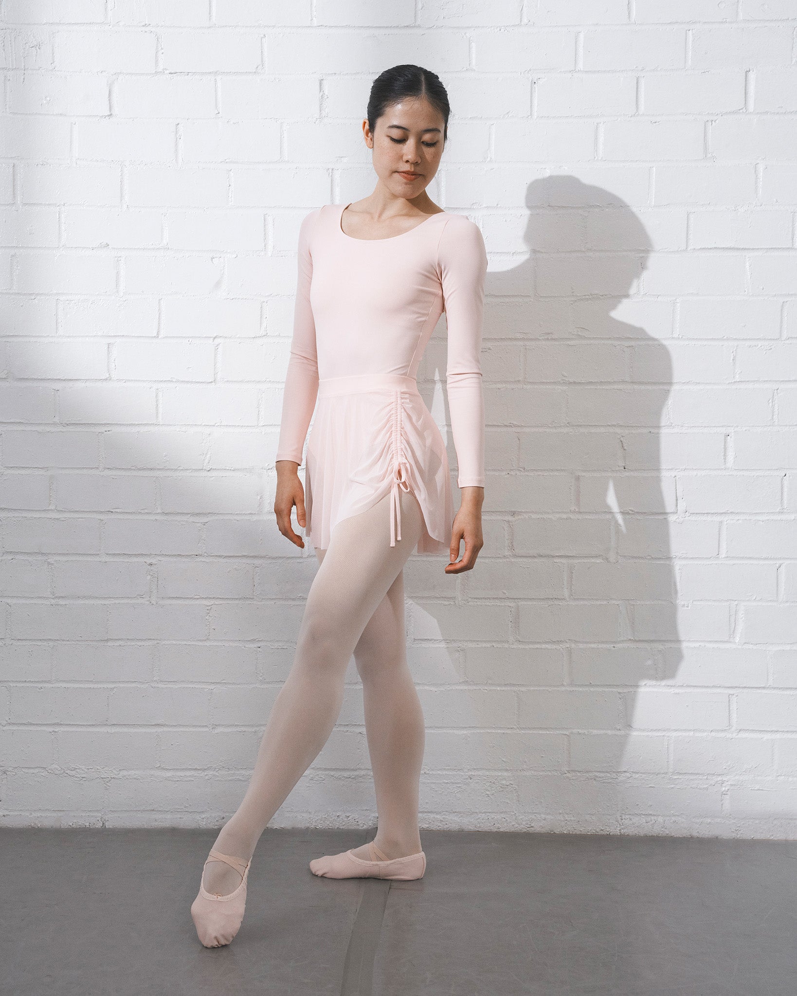Dancer wearing a ballet pink mesh dance skirt with adjustable side ruching over a matching ballet outfit.