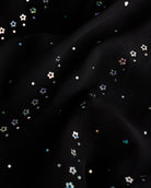 Close-up of black dance dress fabric with sparkling floral sequins on chiffon for a playful ballet performance look.