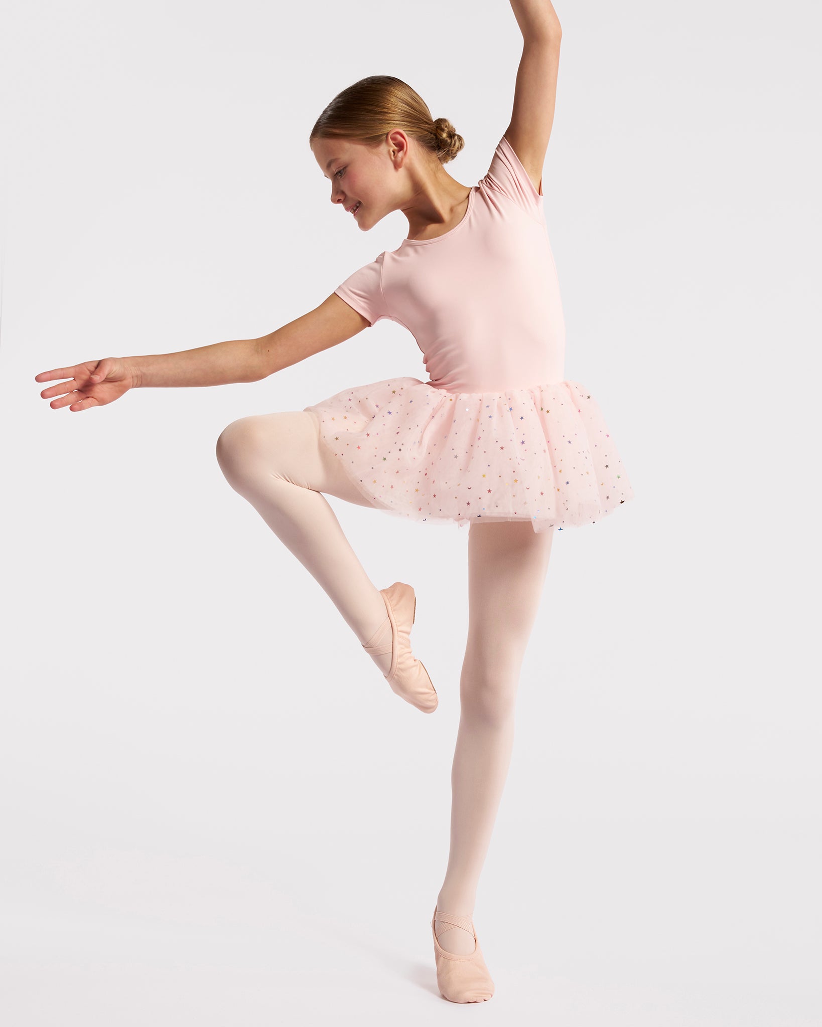 Young dancer wearing a ballet pink celestial sequin tutu dress while posing in ballet shoes and pink tights.