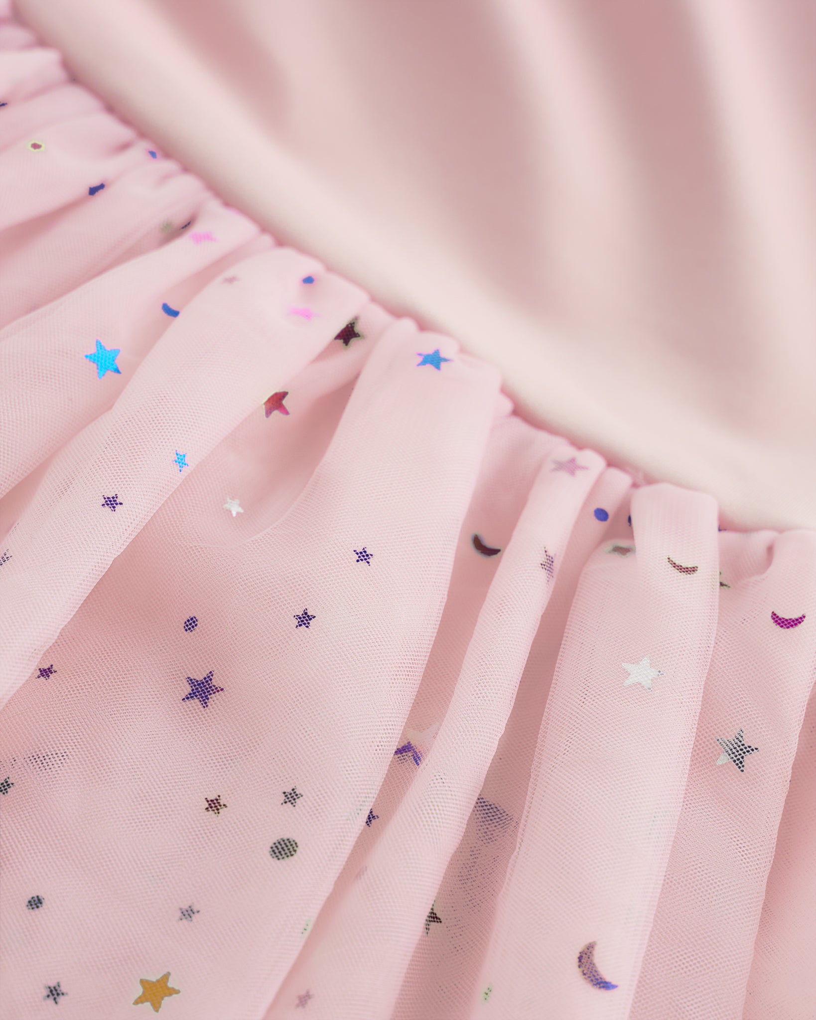 Close-up of ballet pink tutu dress skirt showing multicolor celestial sequins, layered mesh, and star and moon details.
