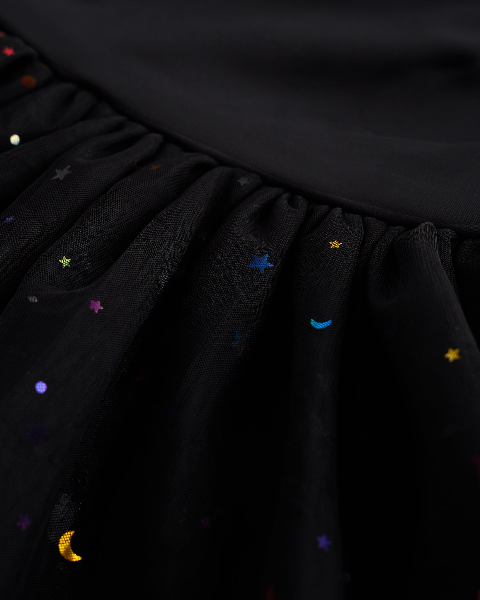 Close-up of black tutu dress skirt showing multicolor celestial sequins, layered mesh, and star and moon details.