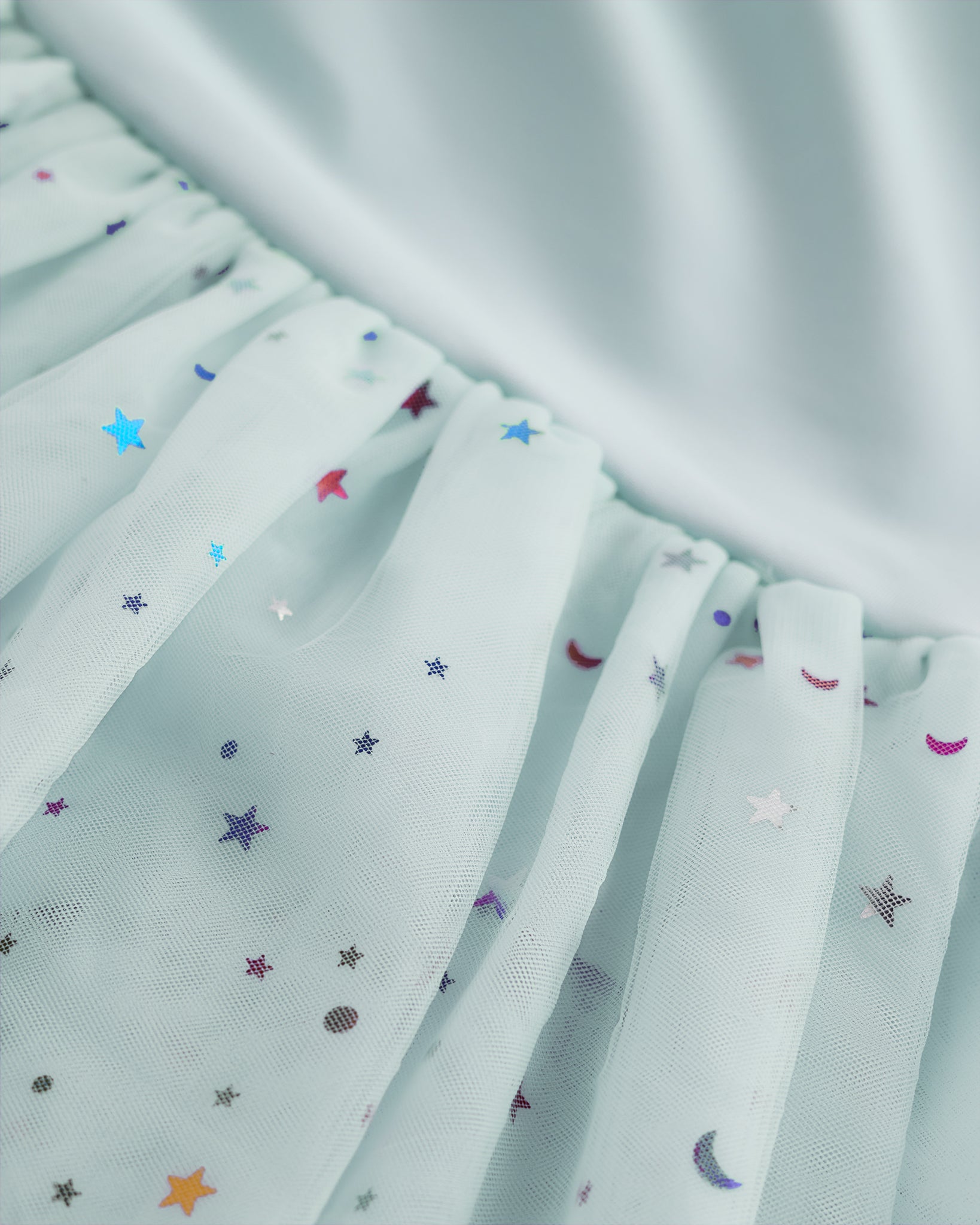 Close-up of blue tutu dress skirt showing multicolor celestial sequins, layered mesh, and star and moon details.